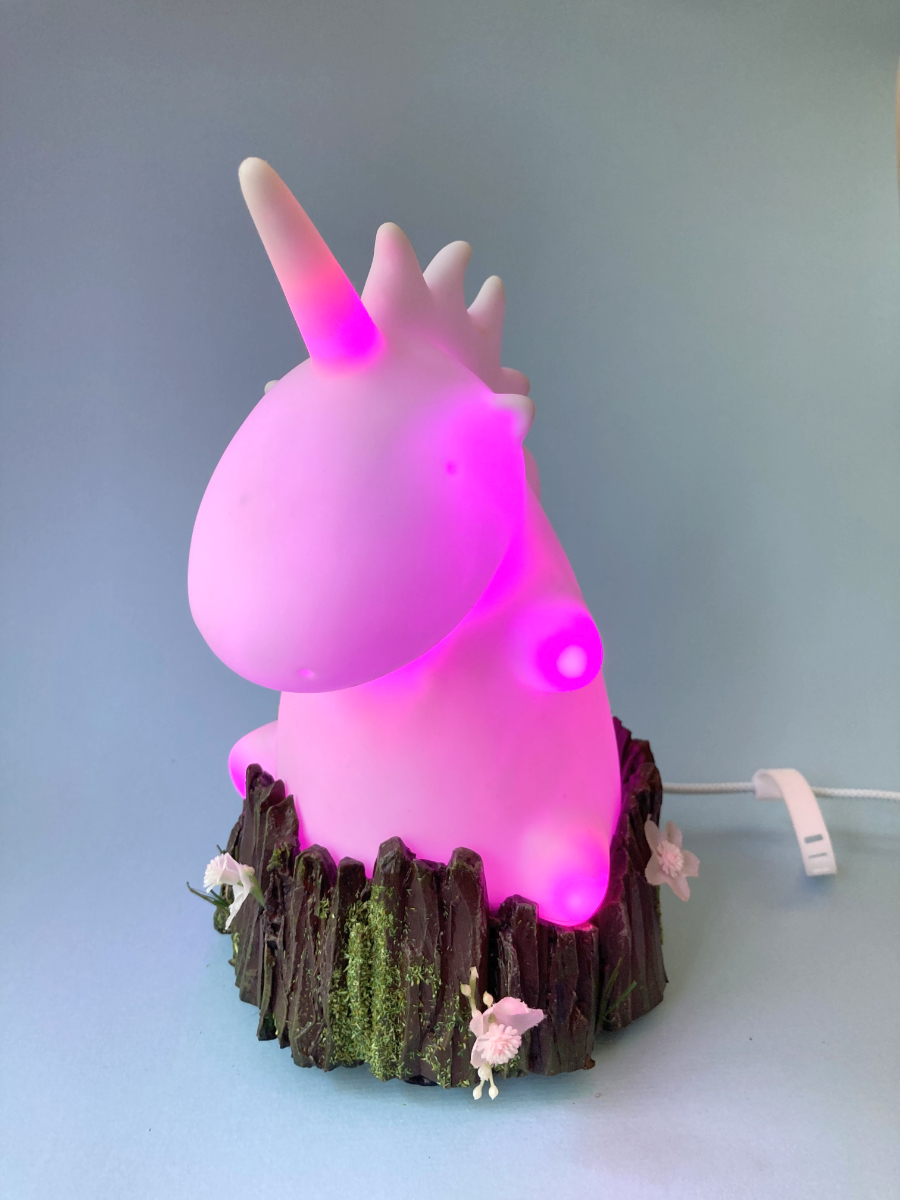 Van binnenuit roze verlichte plastic eenhoorn op een boomstronk